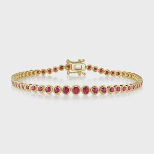 May include: A gold bracelet featuring a series of round, vibrant red gemstones. The bracelet has a delicate design with a secure clasp. The gemstones are evenly spaced along the gold band, creating a continuous line of color.