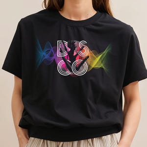 Könnte beinhalten: Schwarzes T-Shirt mit farbenfrohem Grafikdesign. Das Design zeigt das Wort "DISCO" in Weiß, eine Silhouette einer tanzenden Person und farbige Wellenlinien. Das T-Shirt hat einen Rundhalsausschnitt.