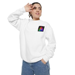 May include: A white long-sleeve crewneck sweatshirt featuring a small black square patch on the left chest. The patch contains a vibrant, multi-colored rainbow triangle graphic with a glowing, prismatic effect against a dark background.