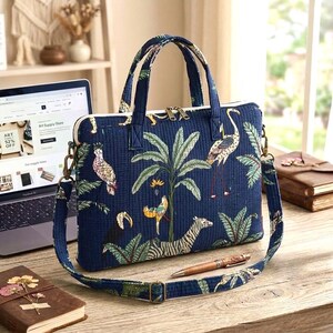 Puede incluir: Bolso para portátil azul marino con estampado tropical con cebra, pájaros y palmeras. El bolso tiene una asa superior y una correa para el hombro desmontable. Un portátil está abierto en el fondo.