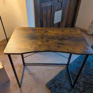 May include: A rectangular desk with a dark brown, wood-look surface and black metal legs. The desk has a curved front edge and is suitable for home or office use. The desk is approximately 47 inches wide and 24 inches deep.
