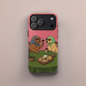 May include: A pink iPhone case with a design of two dogs in sunglasses and headscarves, drinking wine and eating cheese. The dogs are at a table with a green cloth, a cheese board, and a bowl of olives.