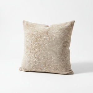 May include: A square beige decorative pillow with a swirling, textured pattern. The pillow has a soft, plush appearance and is likely made of a comfortable fabric. The design is symmetrical, creating a visually appealing accent for home decor.