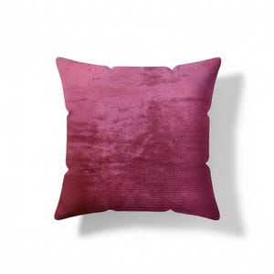May include: A square decorative pillow in shades of pink and magenta. The pillow has a textured, velvet-like appearance. The color gradient transitions from a lighter pink at the top to a deeper magenta at the bottom. The pillow is a home decor item.