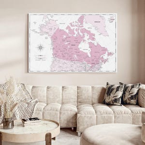 May include: A rectangular wall art print featuring a detailed map of Canada and surrounding regions in shades of soft pink and white. The map includes geographical labels, a compass rose, and the text The World Awaits printed in the lower left corner.
