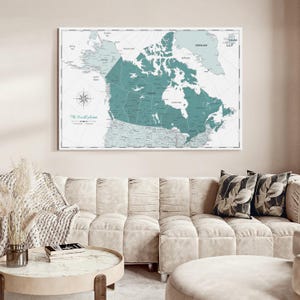 May include: A rectangular wall map of Canada featuring a teal-colored landmass against a light gray background. The map includes a compass rose in the lower-left corner and the text The World Awaits printed in a script font below the compass.
