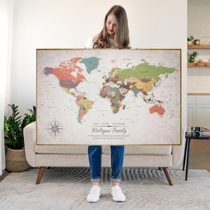 May include: A framed world map with a vintage aesthetic, featuring a compass rose and country outlines in various colors. The map includes the text "Rodriguez Family" and a quote. The frame is gold-colored.