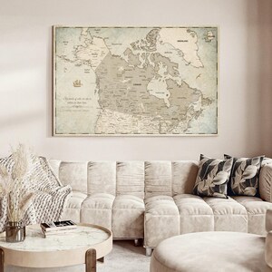 May include: A rectangular wall map of Canada and surrounding regions in muted beige and blue tones. The map features detailed geographical labels, a compass rose, and a small ship illustration. The text "So much of who we are is where we have been" is printed on the left side of the map.