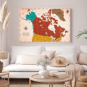 May include: A rectangular wall map of Canada featuring a color-blocked design with teal, deep red, and mustard yellow sections. The map includes a compass rose, geographic labels, and text that reads "THE JOURNEY STILL IS ON" and "Travels & Adventures".
