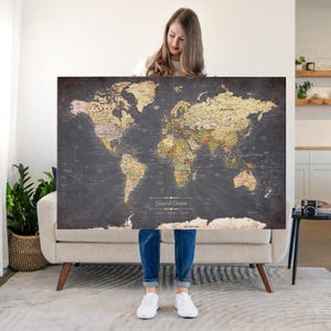 May include: A large rectangular world map poster featuring a dark charcoal gray background with continents depicted in shades of beige, tan, and muted green. The text "Gatrad & Charlotte" is printed in white in the lower center area.
