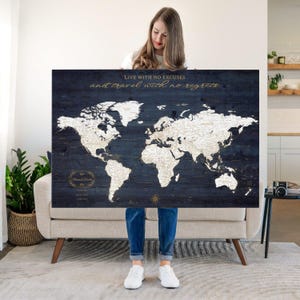 May include: A large rectangular world map printed on dark blue wood planks. The map features white continents with gold text accents. The top center displays the text "LIVE WITH NO EXCUSES and travel with no regrets." A gold compass rose is at the bottom.