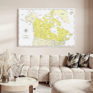 May include: A rectangular wall map print featuring a pale yellow and white color scheme. The map displays the geography of Canada, Greenland, and Alaska with black text labels for cities and regions. A compass rose is located on the left side.