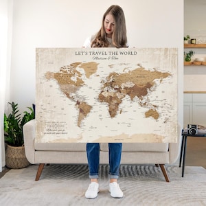 May include: A large rectangular world map poster with a beige background and brown continents. The text reads LET'S TRAVEL THE WORLD, Madison & Tom, and OUR ADVENTURES Wherever you go, go with all your heart. The map features country names.