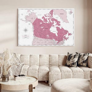 May include: A rectangular wall map featuring a pink and white color scheme, centered on Canada with surrounding regions visible. The map includes a compass rose, grid lines, and the text The World Awaits printed in the lower left corner area.