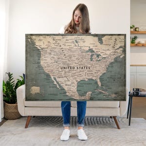 May include: A large rectangular wall map of North America featuring a muted color palette of beige and dark teal. The map displays detailed geographical labels for the United States, Canada, and Mexico, with the text UNITED STATES centered.