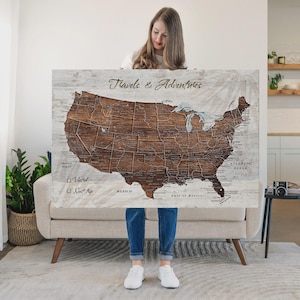 May include: A rectangular wall map of the United States featuring a dark brown wood grain finish for the landmass and a light, weathered white wood background. The text "Travels & Adventures" is printed at the top, with "Visited" and "Next Trip" checkboxes.