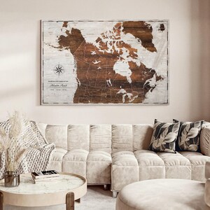 May include: A rectangular wall art piece featuring a map of North America printed on a wood-grain background. The map displays dark brown landmasses against a light wood-toned ocean. It includes a compass rose and the text Adventure Awaits.