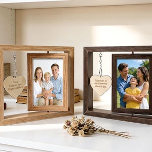 Pode incluir: Duas molduras de madeira, uma castanho-claro e outra castanho-escuro, cada uma com uma foto e um adorno pendurado em forma de coração. A moldura castanho-claro tem o texto "Your Custom Text Engraved Here" no coração. A moldura castanho-escuro tem o texto "Together is our favorite place to be."
