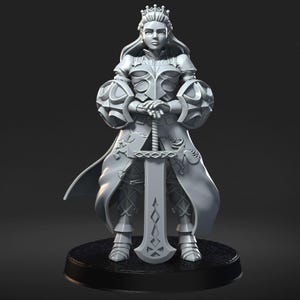 May include: A gray figurine of a woman in armor, holding a sword. The figure wears a crown and a long coat with decorative patterns. The figurine stands on a black circular base, with a dark background.