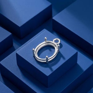 Könnte beinhalten: Eine silberfarbene, ovale Anhängerfassung mit einem glatten, polierten Metallrahmen und vier Krappen, die dazu dienen, einen Edelstein zu halten. Die Fassung verfügt über eine kleine, runde Öse an der Oberseite zur Befestigung an einer Kette.