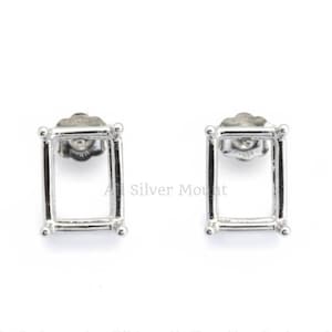 May include: Two silver rectangular stud earrings. Each earring has a simple, open frame design with rounded corners and a post backing. The earrings are displayed on a white background.