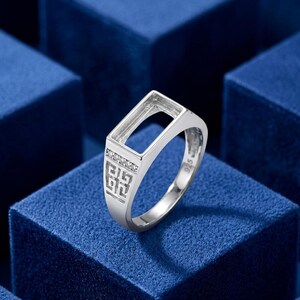 May include: A silver ring featuring a rectangular setting for a stone, accented with small clear stones along the band. The side of the band displays a geometric cut-out pattern, and the interior of the band is clearly stamped with the 925 hallmark.