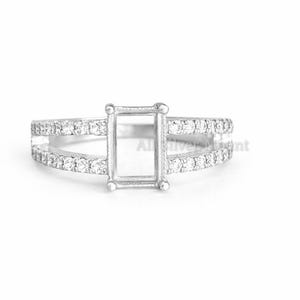 May include: A silver ring with a rectangular center setting and a split band. The band is adorned with small, round, clear stones. The ring is set against a white background, highlighting its design and details.