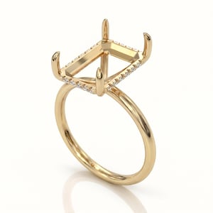 Puede incluir: Un engaste de anillo de oro con un diseño de corte esmeralda, con pequeñas piedras de acento a lo largo de los bordes superiores. El anillo tiene un acabado pulido y un estilo clásico y elegante. El engaste está diseñado para sostener una piedra preciosa.