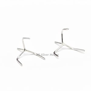 May include: Two silver-colored metal display stands. Each stand has a three-legged base and a curved top. The stands are designed to hold small items. The stands are on a white background.