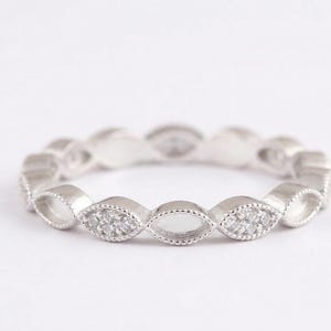 May include: A silver ring with a repeating pattern of marquise-shaped settings. Each setting alternates between clear stones and a cluster of small, sparkling stones. The ring is set against a white background.