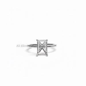 May include: A silver ring with a rectangular setting, designed to hold a gemstone. The ring has a thin band and a detailed setting, perfect for a custom piece. The ring is displayed on a white background.