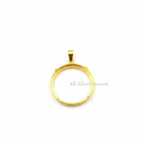 Puede incluir: Un colgante dorado con un marco circular y un pequeño lazo en la parte superior para una cadena. El texto "All Silver Mount" está impreso en el marco. El colgante está diseñado para sostener una piedra o un amuleto redondo.