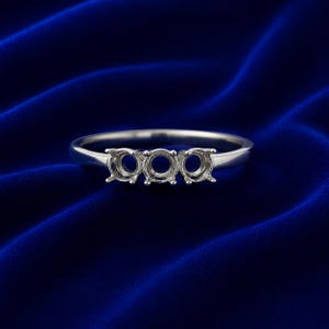 Peut inclure: Une bague en métal argenté dotée de trois griffes circulaires vides disposées sur une ligne horizontale. L'anneau est lisse et poli, conçu pour accueillir trois pierres. Le métal présente une surface réfléchissante et une structure simple.
