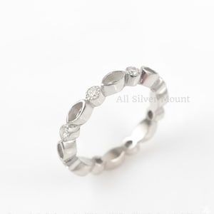 Könnte beinhalten: Ein silberner Ring mit einem sich wiederholenden Muster aus ovalen und runden Formen, die jeweils mit kleinen, klaren Edelsteinen besetzt sind. Der Ring befindet sich auf weißem Hintergrund. Der Text "All Silver Mount" ist sichtbar.