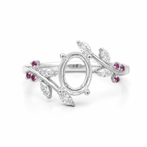 May include: A silver ring featuring an oval setting, embellished with leaf motifs. The leaves are set with clear and pink gemstones. The ring's design is delicate and inspired by nature, suitable for various events.