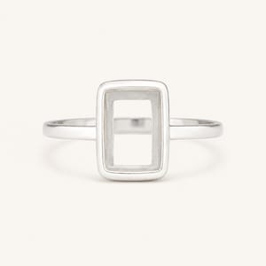 Puede incluir: Un anillo de plata con un engaste rectangular. El anillo presenta un diseño sencillo y moderno con un acabado pulido. El engaste rectangular está vacío, listo para una piedra preciosa u otro adorno. El anillo se muestra sobre un fondo blanco.