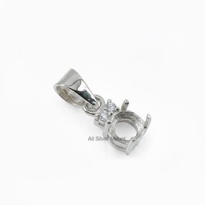Könnte beinhalten: Ein silberner Anhänger mit einer runden Lünette und zwei kleinen Akzentsteinen. Der Anhänger hat eine Schlaufe für eine Kette und ist für einen Edelstein konzipiert. Der Text "All Silver Mount" ist sichtbar.