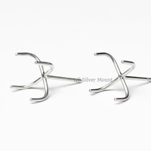 May include: Two silver-colored, prong-style jewelry settings. Each setting has a post and three curved prongs designed to hold a gemstone. The settings are displayed on a white background.