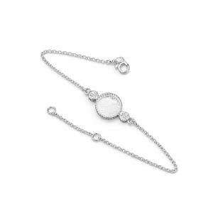 Può includere: Un bracciale d'argento con un delicato design a catena. Il bracciale presenta un'incastonatura circolare centrale e due incastonature rotonde più piccole, tutte adornate da pietre chiare e scintillanti. Il bracciale è regolabile e ha una chiusura a fermaglio.