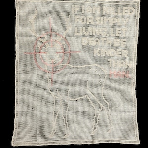 May include: A cream-coloured, crocheted wall hanging featuring a deer silhouette with a pink target over its head. The text reads, "If I am killed for simply living let death be kinder than man."