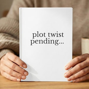 May include: A white book with the text "plot twist pending..." in black. The book is held by a person. The book's cover is clean and simple, with the text centered on the front.