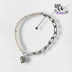 May include: A necklace featuring a combination of white pearls and a silver chain. The necklace has a heart-shaped pendant and the text "Love is Poison" in the upper right corner.