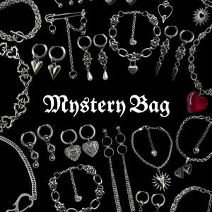 Op de afbeelding: Een collectie zilverkleurige sieraden waaronder diverse kettingen, oorringen met hart- en stekelbedels, veiligheidsspeld-broches en armbanden. De tekst Mystery Bag staat in het midden in een wit gotisch lettertype op een zwarte achtergrond.