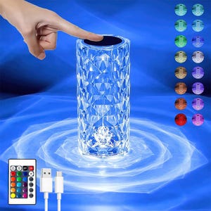 May include: A cylindrical crystal table lamp with a geometric faceted pattern that refracts light. The lamp features a touch-sensitive top panel, a remote control with multiple colour options, and a USB charging cable for power and operation.