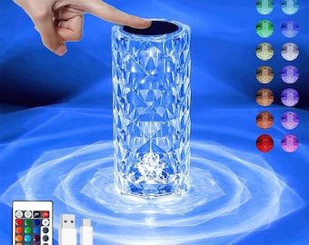 May include: A cylindrical crystal table lamp with a geometric faceted pattern that refracts light. The lamp features a touch-sensitive top panel, a remote control with multiple colour options, and a USB charging cable for power and operation.