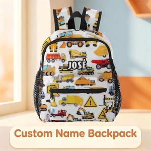 May include: A white backpack featuring a repeating pattern of yellow construction vehicles, road signs, and safety gear. The center of the bag displays the name JOSÉ in bold black capital letters. It includes black zippers and side mesh pockets.