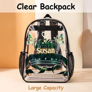 Peut inclure: Un sac à dos transparent avec une impression graphique représentant une couronne vert foncé portant le nom Susan en lettres dorées, entourée de deux papillons irisés et d'un contour de cœur. Il possède des bordures noires et des poches latérales.