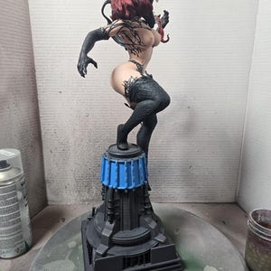Op de afbeelding: Gedetailleerd beeldje van een vrouwelijk personage met een zwart en rood kleurenschema. De figuur is dynamisch geposeerd op een futuristisch ogende basis met blauwe accenten. Het personage heeft ingewikkelde tatoeages en draagt zwarte kleding.