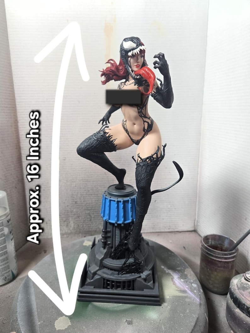 Op de afbeelding: Gedetailleerd beeldje van een vrouwelijk personage, ongeveer 40 cm hoog, met een zwart-wit masker, rood haar en een rode tong. Het beeldje staat op een zwart-blauwe basis, met zwarte accenten en een staart.