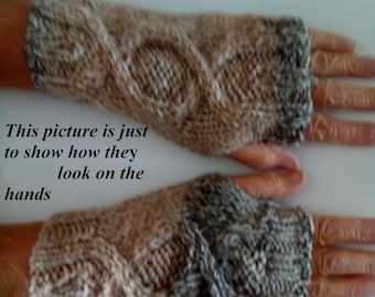 May include: A pair of fingerless gloves featuring a cable knit pattern in a variegated yarn blend of tan, brown, and grey tones. The knit fabric has a textured appearance with a ribbed cuff edge, covering the wrist and palm area while leaving fingers exposed.